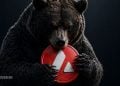Close-up of a dark bear embracing a red circular sign with a white diagonal stripe against a dark background.