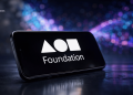 Tilted smartphone showing the Foundation logo on a dark reflective surface with a colorful bokeh background.
