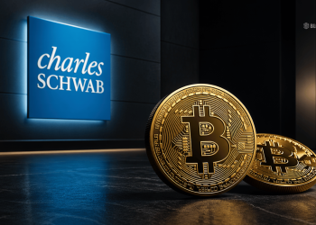 Gold Bitcoin coins on a dark floor with a blue Charles Schwab sign in the background.