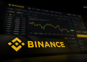 Binance logo in yellow on a dark surface with a blurred cryptocurrency price chart in the background