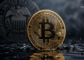 Golden Bitcoin coin with circuitry detail on a reflective surface; blurred U.S. Federal Reserve seal in the background.