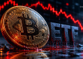 Close-up of a gold Bitcoin coin with circuit-like engravings, set against a red downward-trending market chart in the background