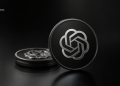 Close-up of a black coin with a silver intertwined knot emblem on a dark reflective surface; blurred stacked coins in the background.