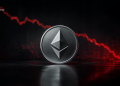 Ethereum coin with geometric logo on a dark reflective surface, red fluctuating chart in the background