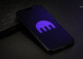 Close-up of a smartphone with a purple glowing logo on its screen, resting on a dark surface, with a Blocknews watermark in the corner.