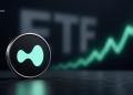 Close-up of a crypto coin with a teal emblem on a dark surface, with a rising green chart in the blurred background.