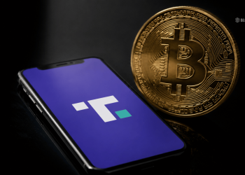 Close-up of a gold Bitcoin coin beside a smartphone screen showing the Flutter logo on a purple background.