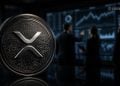 Close-up of an XRP Ripple coin with a circuit-like texture in focus; traders and stock charts blur in a dark trading room behind it.