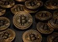 Pile of gold Bitcoin coins scattered on a dark surface, with a prominent central BTC coin and intricate circuit-like designs