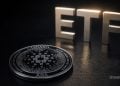 Close-up of a Cardano (ADA) coin on a dark surface with large metallic letters spelling 'ETF' in the background.