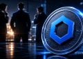 Close-up of a large futuristic coin with a blue hexagonal logo in the foreground; blurred professionals in business attire discuss in a nighttime cityscape background.