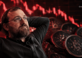 Man with glasses reclining with hands behind head, against a red stock-market background and coin-like discs in the foreground.