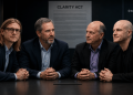Four men in suits sit at a conference table, hands folded, discussing in a dimly lit room with a CLARITY ACT poster in the background.