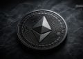 Close-up of a metallic Ethereum coin on a dark textured surface with a geometric logo in the center.