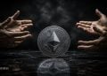 Ethereum coin centered between cupped hands in a dark studio, conveying protection of crypto assets.