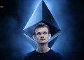 Young man with a large blue geometric diamond hovering around his head in a smoky blue studio; BLOCKNEWS logo in the top-left corner.