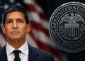 Portrait of a man in a dark suit and tie on the left, with a large U.S. Federal Reserve seal on the right and a blurred American flag in the background.