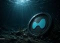 Large circular crypto coin with a blue wave-like symbol rests on the ocean floor, illuminated by sunlit water.