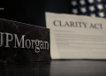 Close-up of a JPMorgan name plaque in the foreground with a blurred 'Clarity Act' document and US flag in the background.