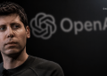 Close-up of a man looking to the left, with a blurred OpenAI logo in the background.
