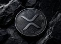 Ripple/XRP coin on a dark, textured rock surface; sleek metallic details visible, BLOCKNEWS watermark in corner (informational image).