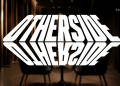 A bold, white, warped 3D wordmark fills the frame against a dark backstage setting with chairs visible in the background.