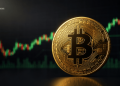 Close-up of a gold Bitcoin coin with a glowing B symbol, over a green/red stock chart background with the BLOCKNEWS logo nearby.