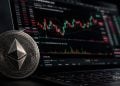 Close-up of an Ethereum coin in front of a computer screen showing candlestick stock charts. (informative)