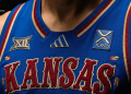 Close-up of a blue Kansas basketball jersey showing embroidered 'KANSAS' lettering and team logos on the chest.