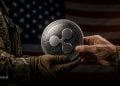 Soldier hands a Ripple cryptocurrency coin to another person, with the U.S. flag in the background.