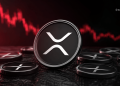 Close-up of a Ripple (XRP) coin with the logo, red market chart in the background and other coins on a dark surface.