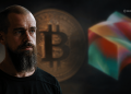 Portrait of a bearded man facing left, with a large Bitcoin coin and a colorful abstract shape blurred in the background.
