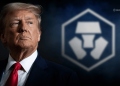 Donald Trump in a navy suit and red tie, facing left, with a blurred blue emblem in the background.